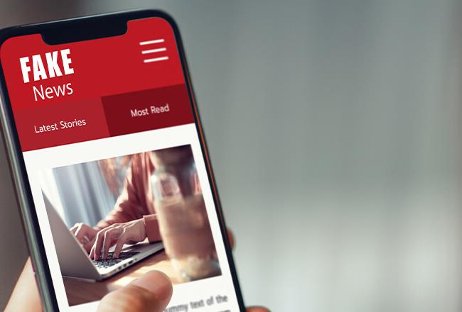 A smartphone displays a news site with a large headline about fake news, along with typical website elements like images and menus.